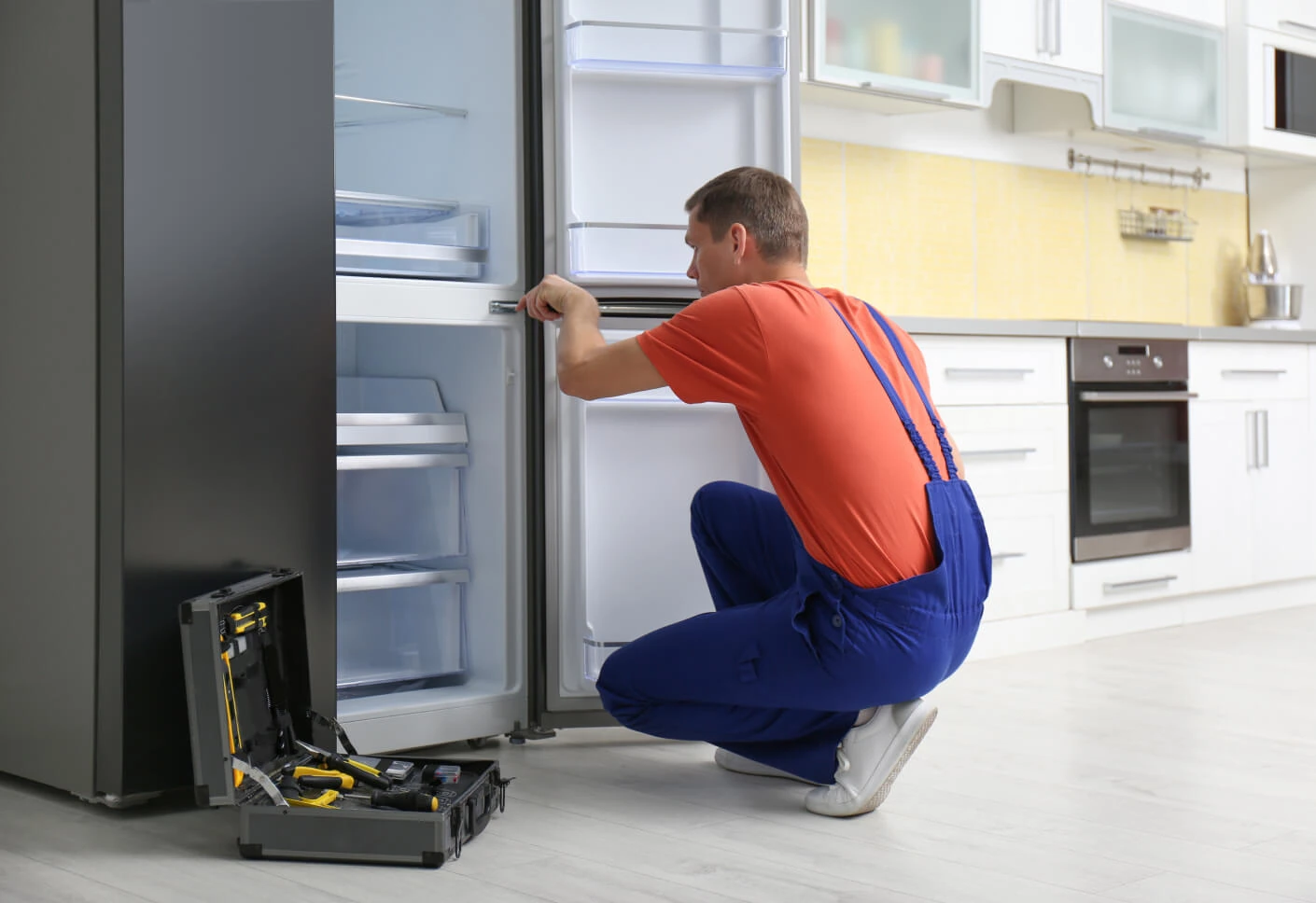 Appliance technician examining an open refrigerator in a bright residential kitchen