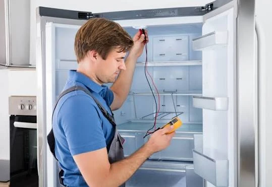 Technician testing the interior of an open refrigerator with a multimeter